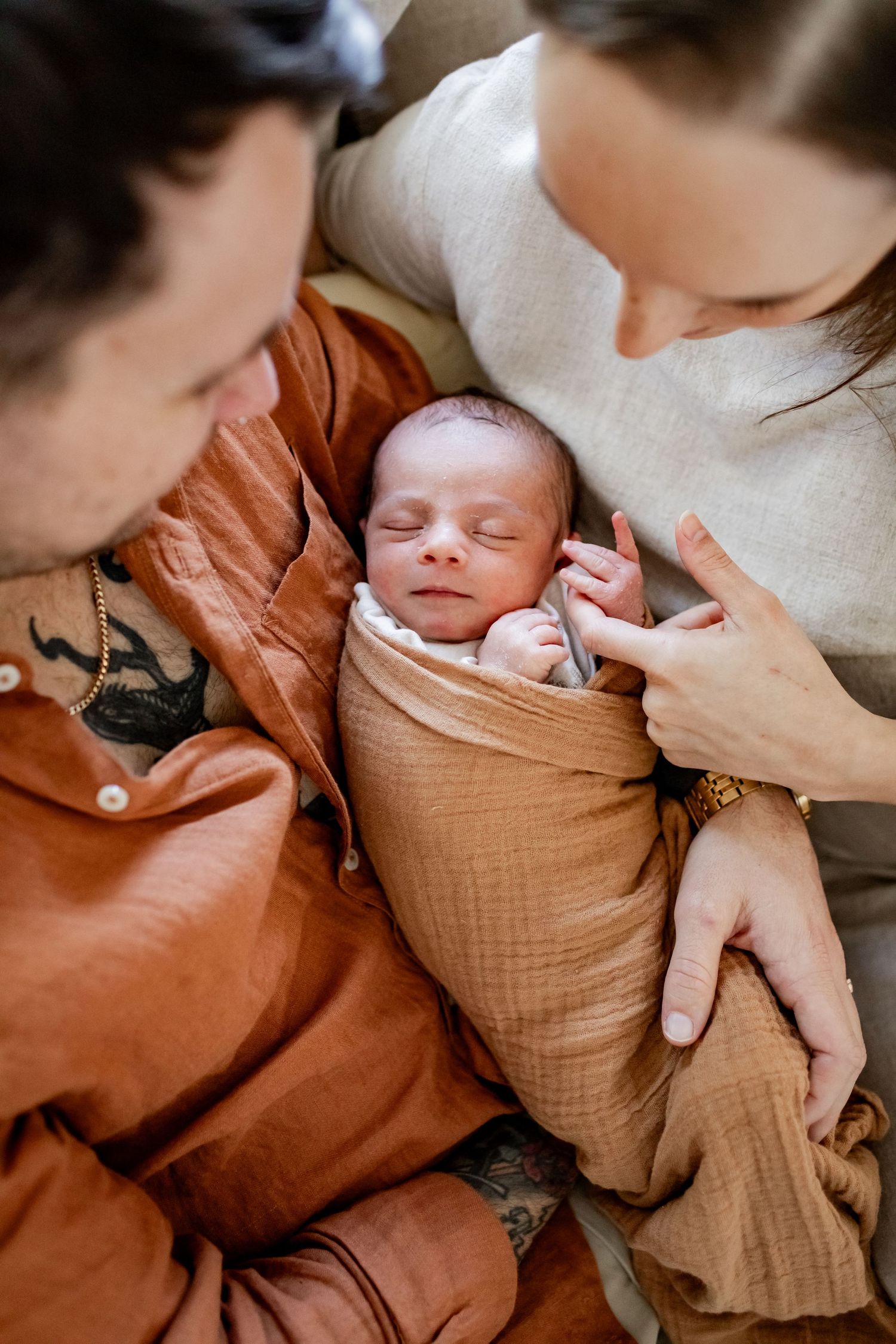 Close-up shot of sleeping newborn wrapped in tan swaddle with parents.