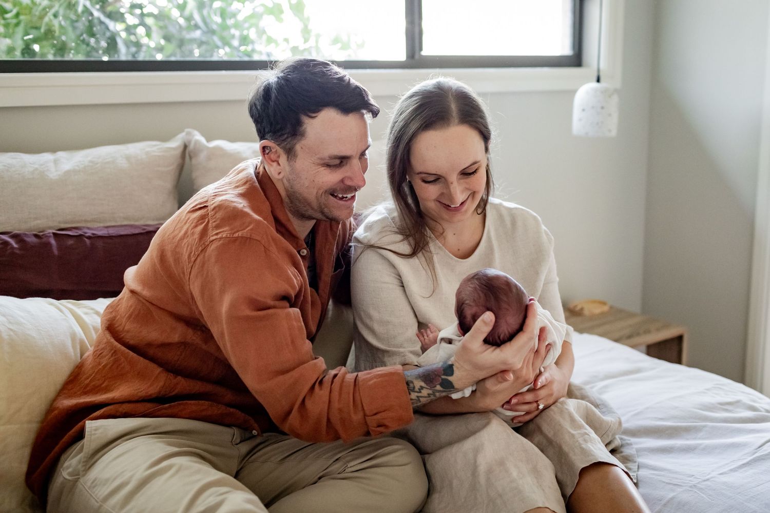 Intimate lifestyle portrait of new parents cuddling with newborn on bed.