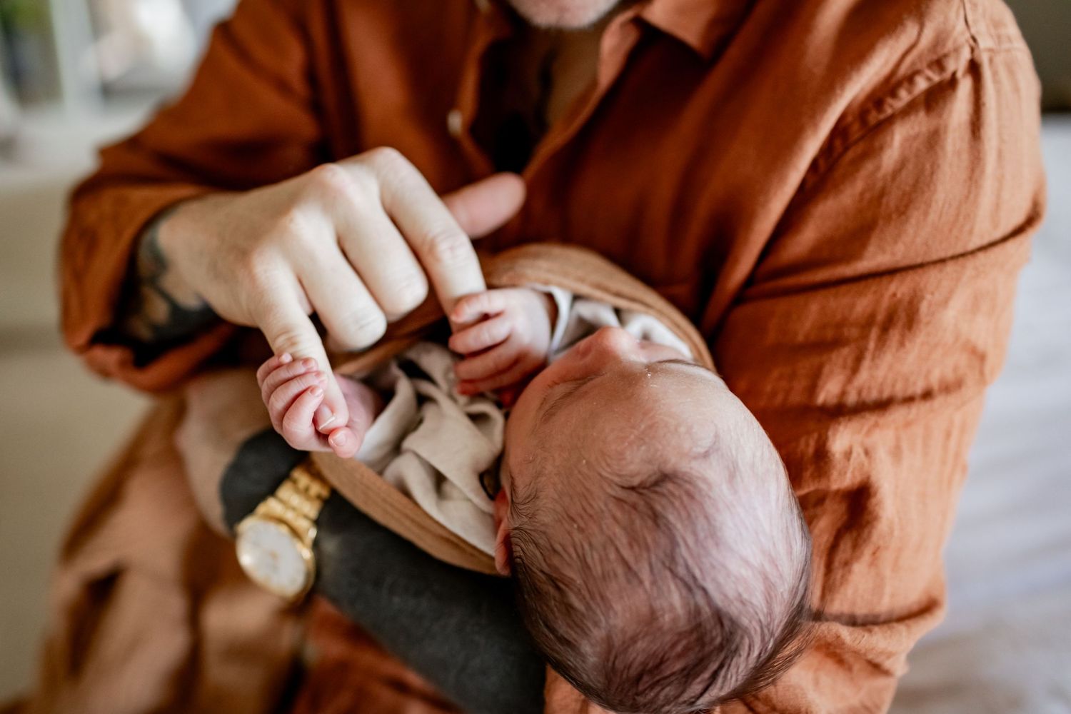 A swaddled sleeping newborn being cradled while wearing brown wrap in natural light.