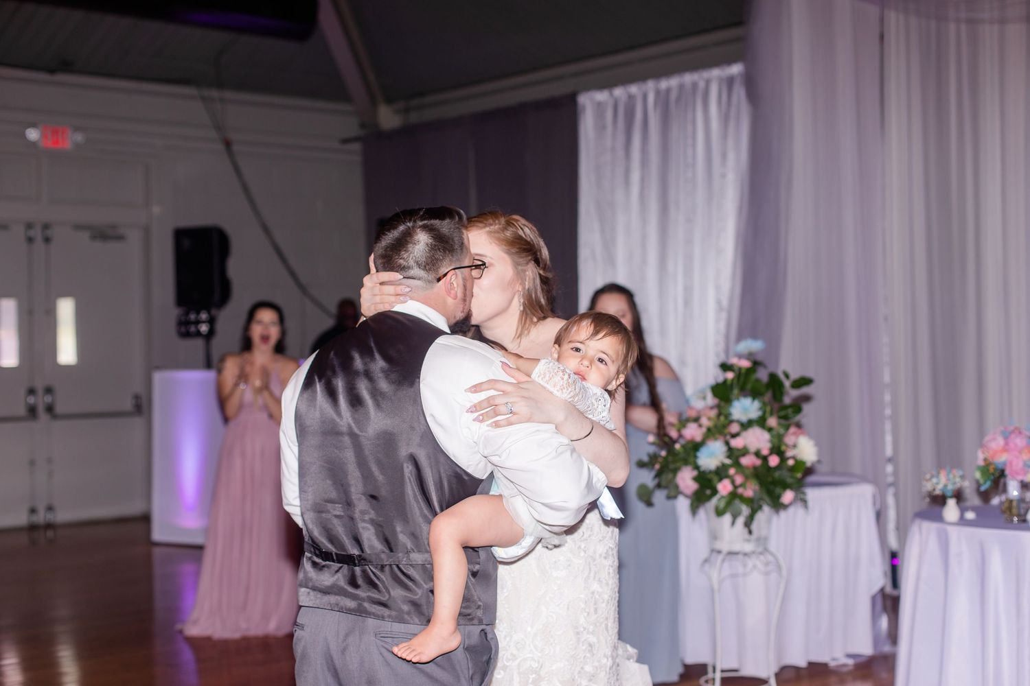 Wedding reception venue decorated with white drapes and purple accent lighting.