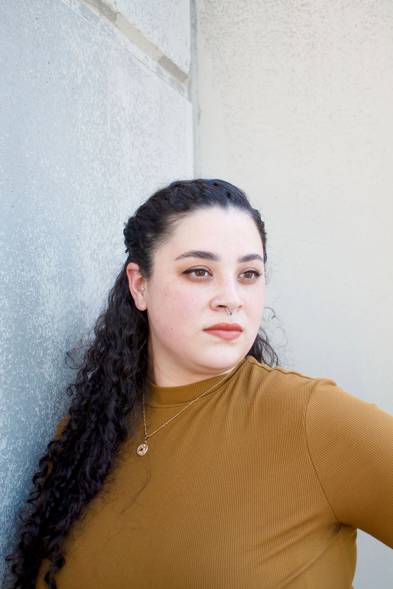 Side profile portrait of someone in a mustard sweater against a white wall.