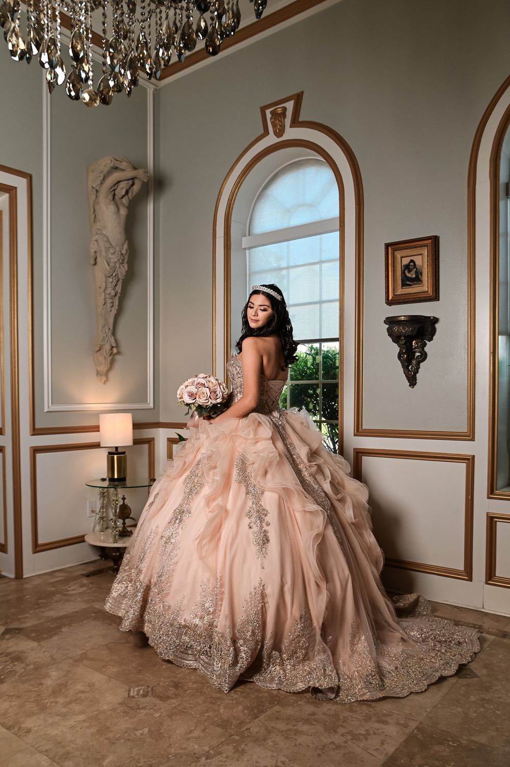 Ornate ballgown with beaded details against elegant architectural elements and chandelier lighting.