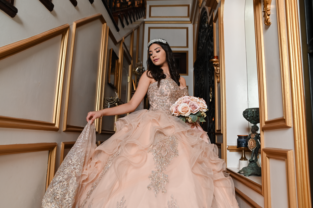 A dramatic staircase photo showcasing a flowing blush pink ballgown with intricate beadwork.