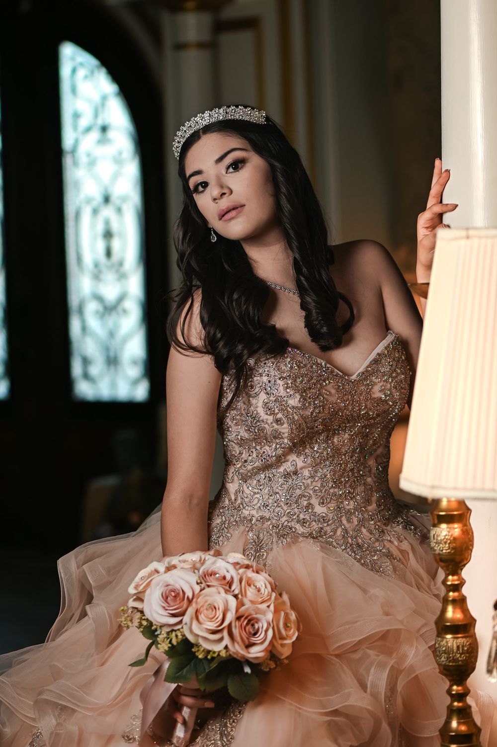 A formal portrait showing a sparkling beaded gown and delicate rose bouquet against an ornate backdrop.