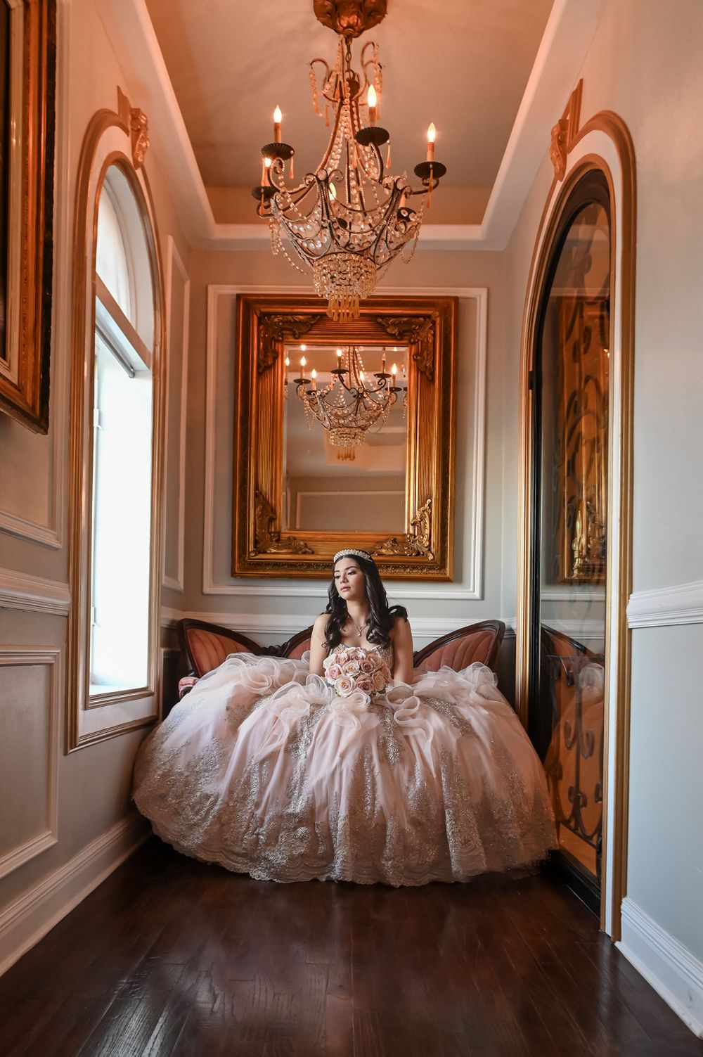 A regal portrait in an elegant hallway featuring a chandelier and full pink princess gown.