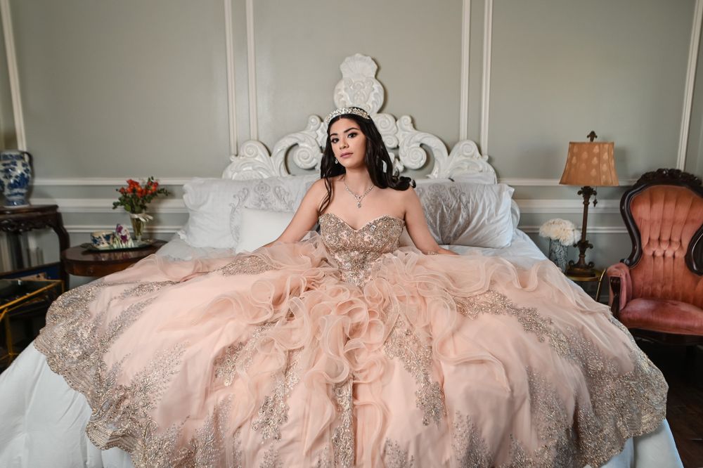 A dreamy bedroom portrait showcasing an ornate pink ballgown against an elegant white headboard.