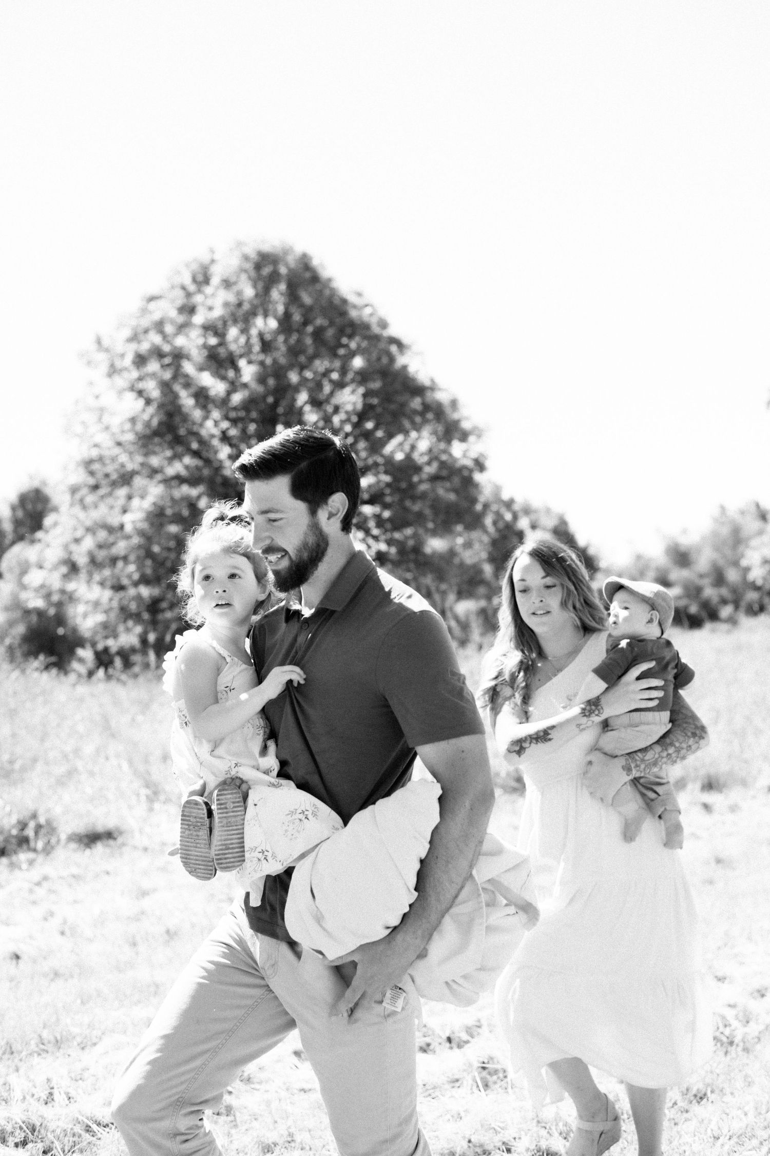 A black and white family portrait taken in a sunlit meadow.