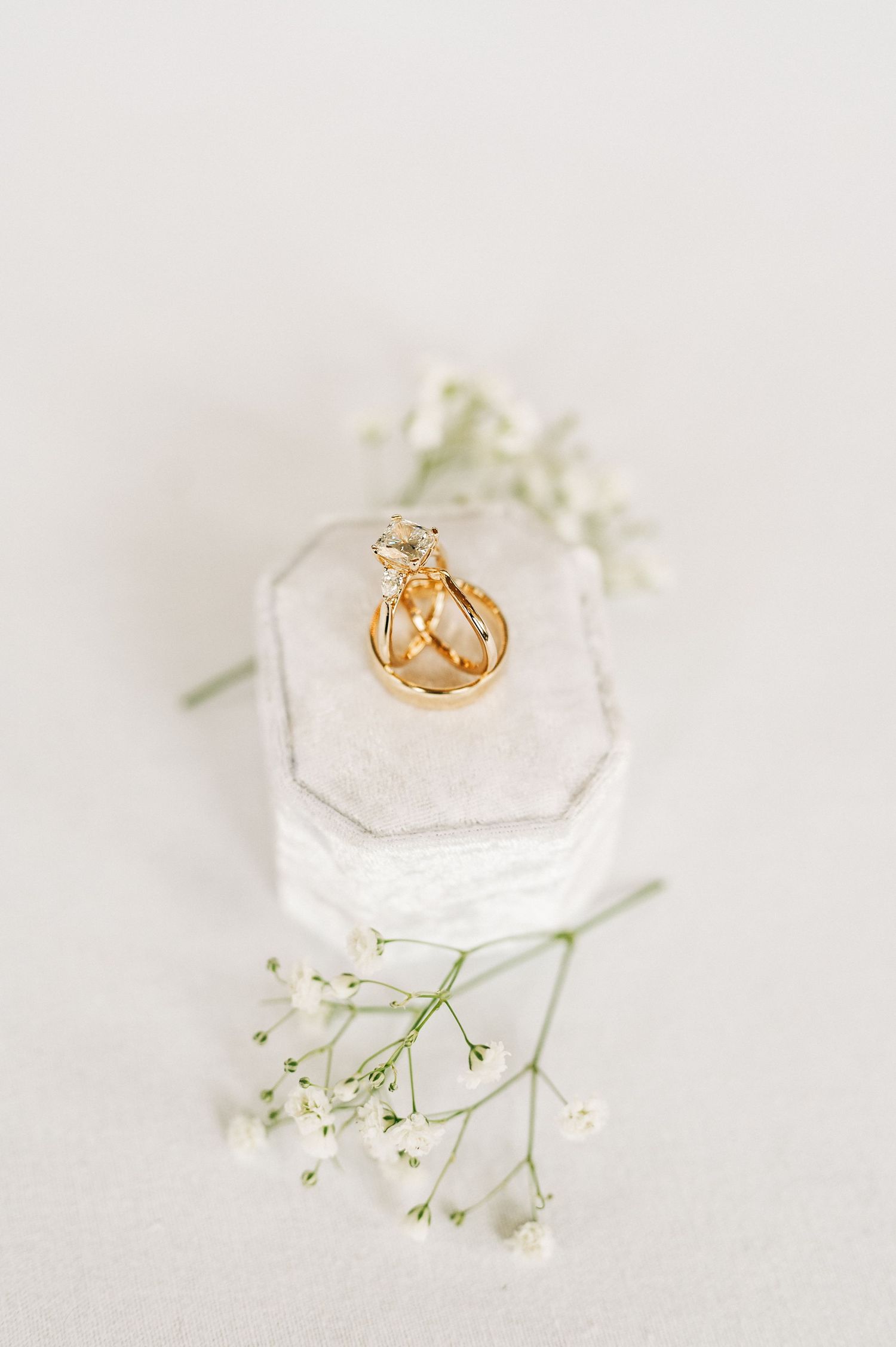 Gold wedding rings displayed on white geometric box with delicate baby's breath flowers.