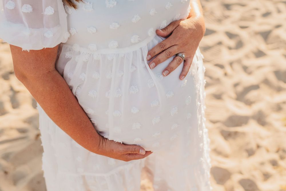 Multiple shots of hands tenderly touching a pregnant belly in white dress on sandy beach.