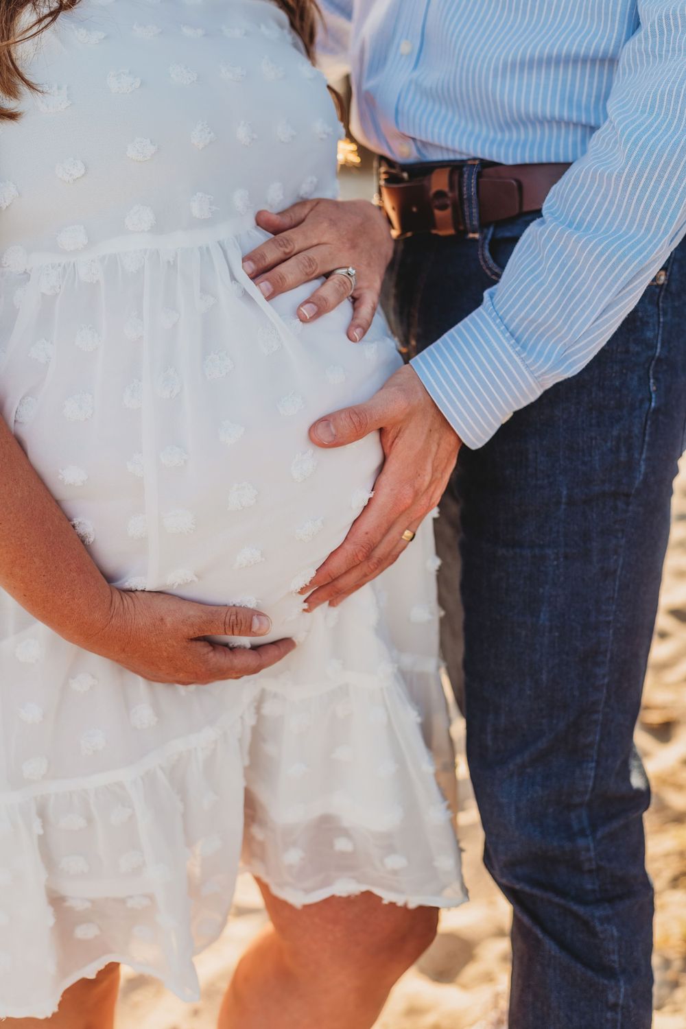Close-up series of hands gently cradling pregnant belly in white dress.