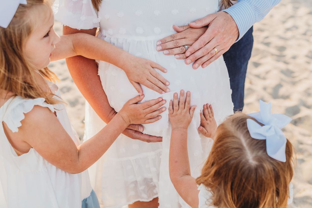 Close-up shots of hands touching a pregnant belly in white dress on beach.