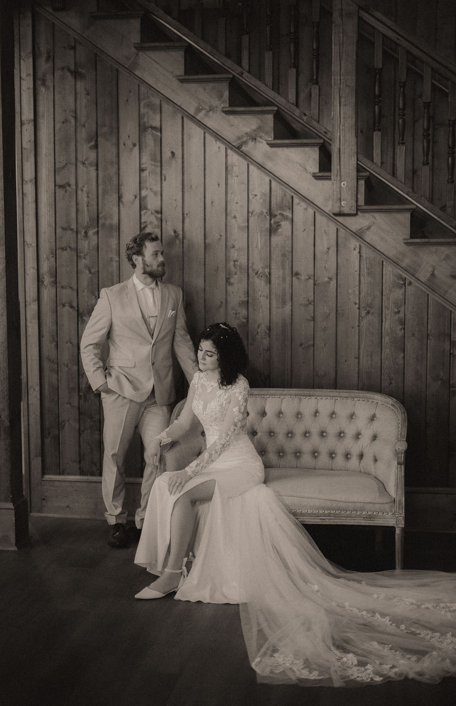Black and white wedding photos showing couple posing by vintage tufted couch and wooden staircase.