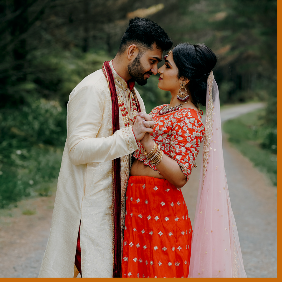 indian couple in traditional wedding attire posing in the driveway of a forest