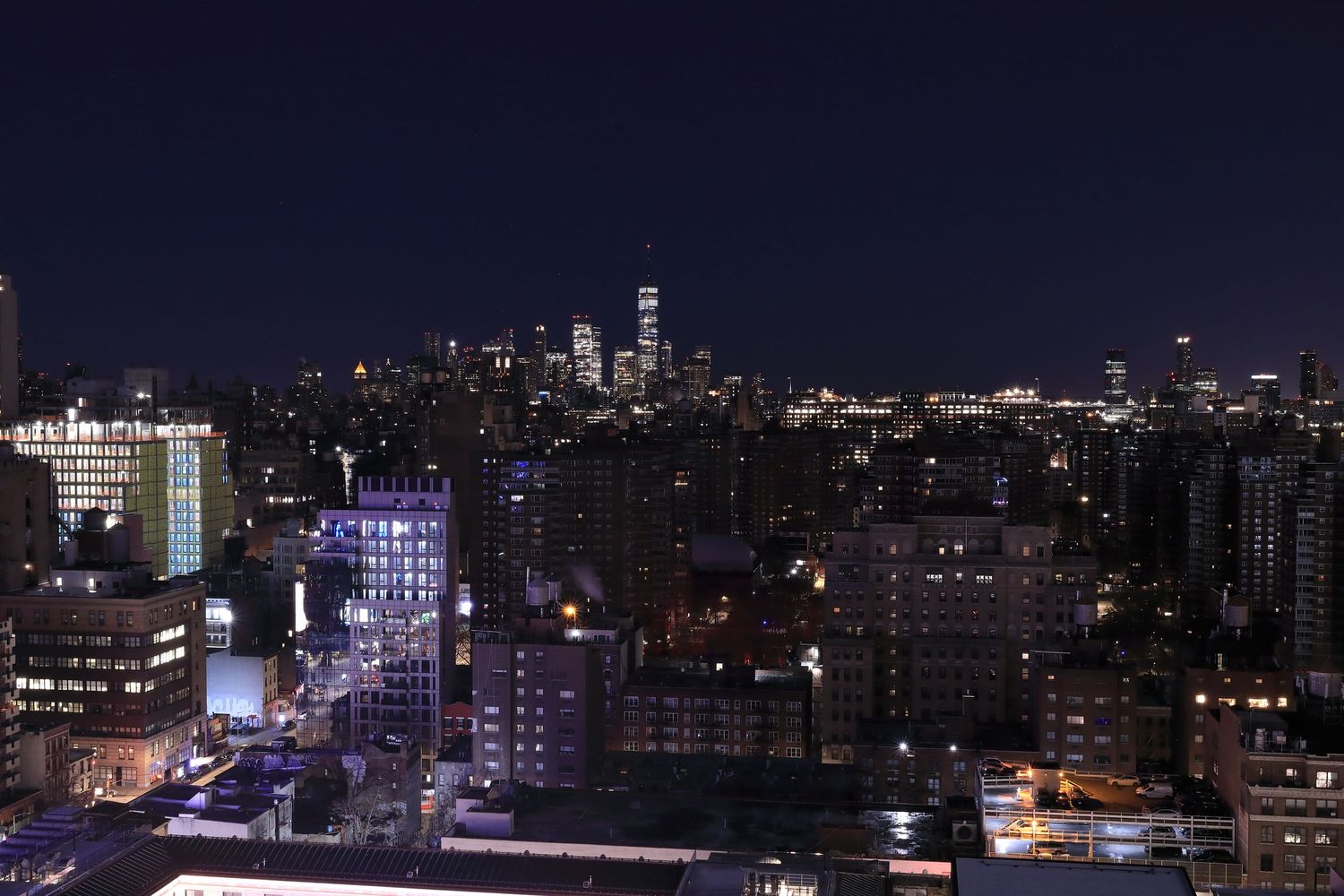 Manhattan skyline at night with illuminated skyscrapers and city lights.