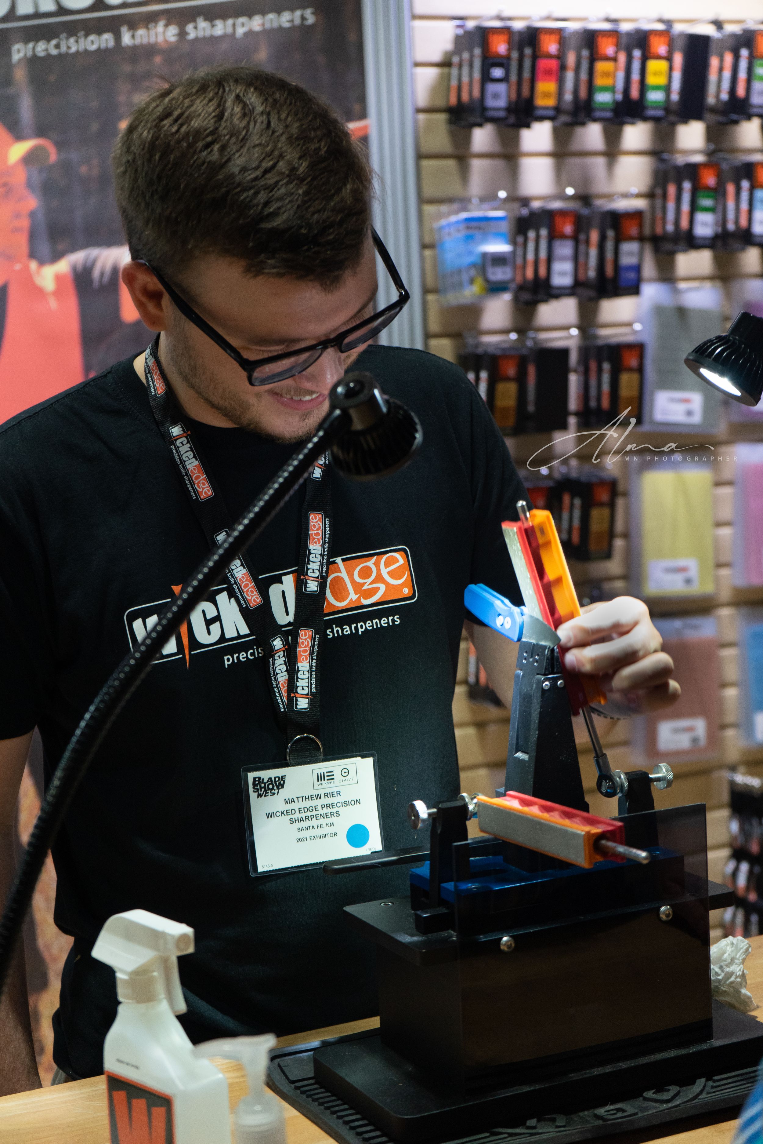Knife sharpening demonstration at retail display with professional equipment and tools.