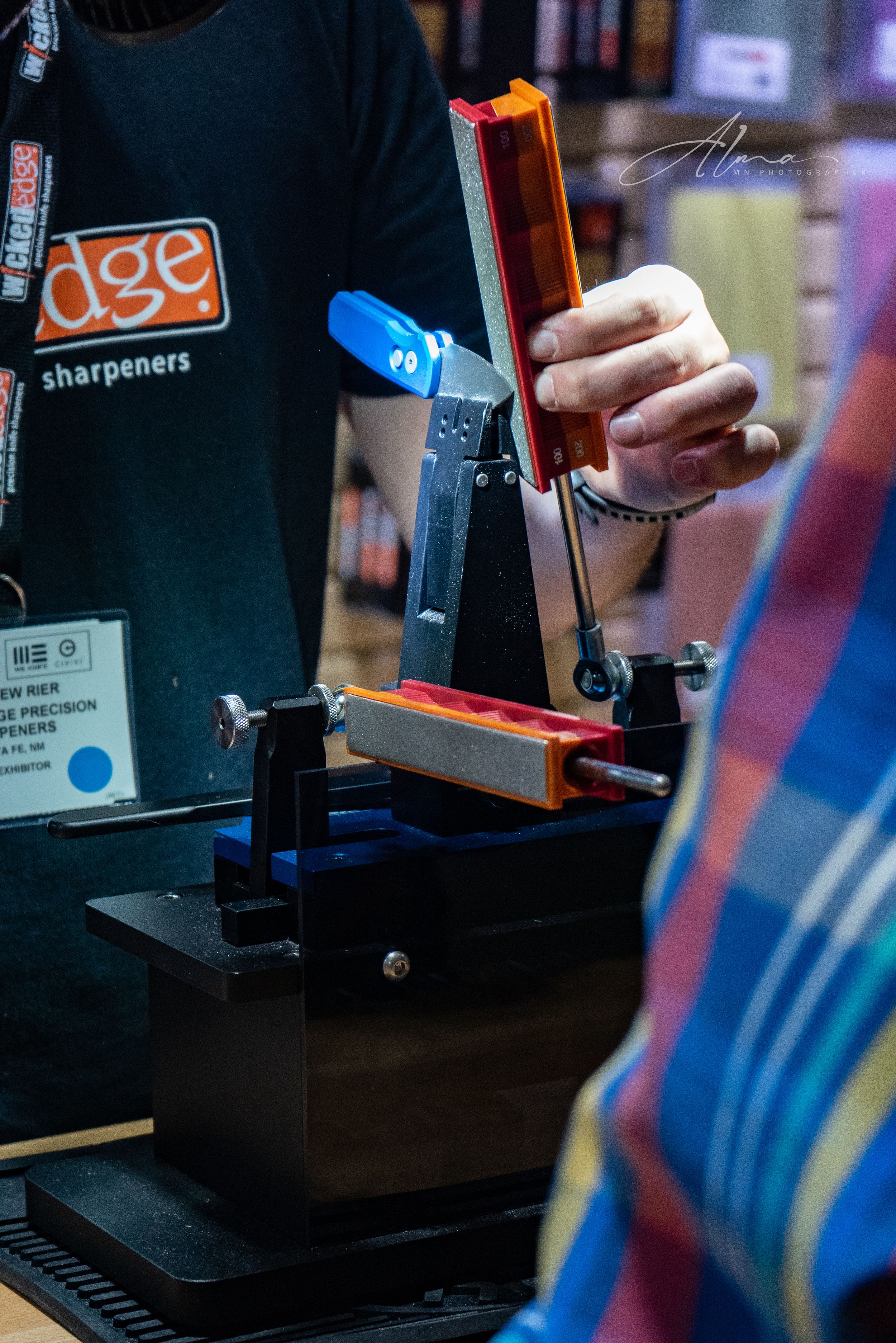 Close-up of knife sharpening system with orange and blue components on black stand.