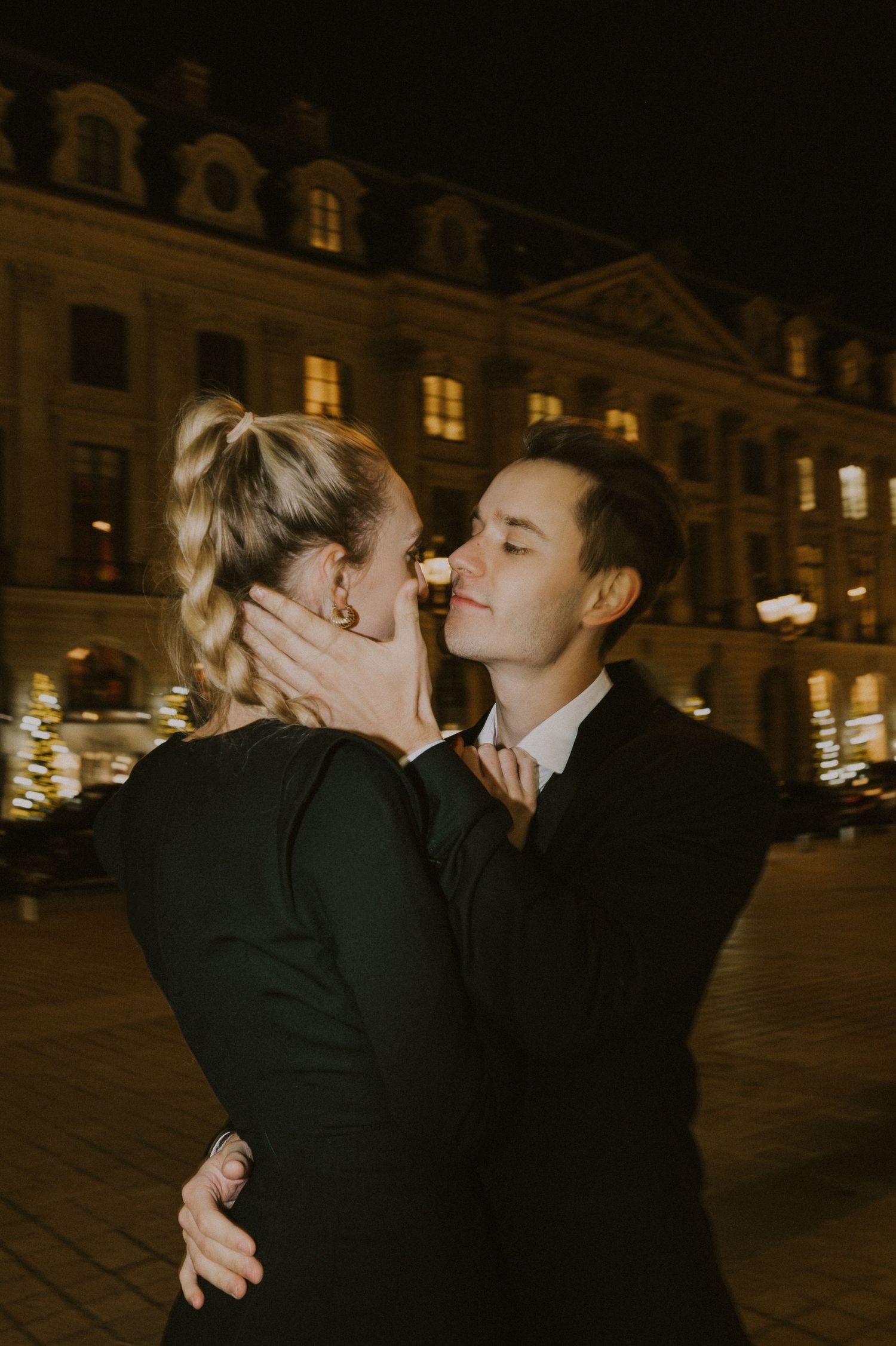 Romantic nighttime embrace in front of illuminated historic building in Paris.