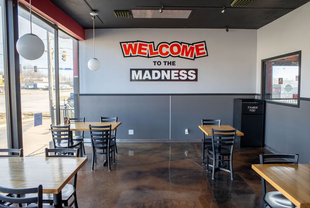 Empty restaurant interior with Welcome to the Madness sign on gray wall and scattered dining tables. Quad Cities Real Estate Photography