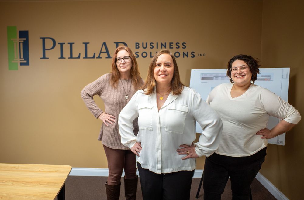 Three professionals standing in an office with Pillar Business Development signage on the wall. Quad Cities Business Headshot Photography