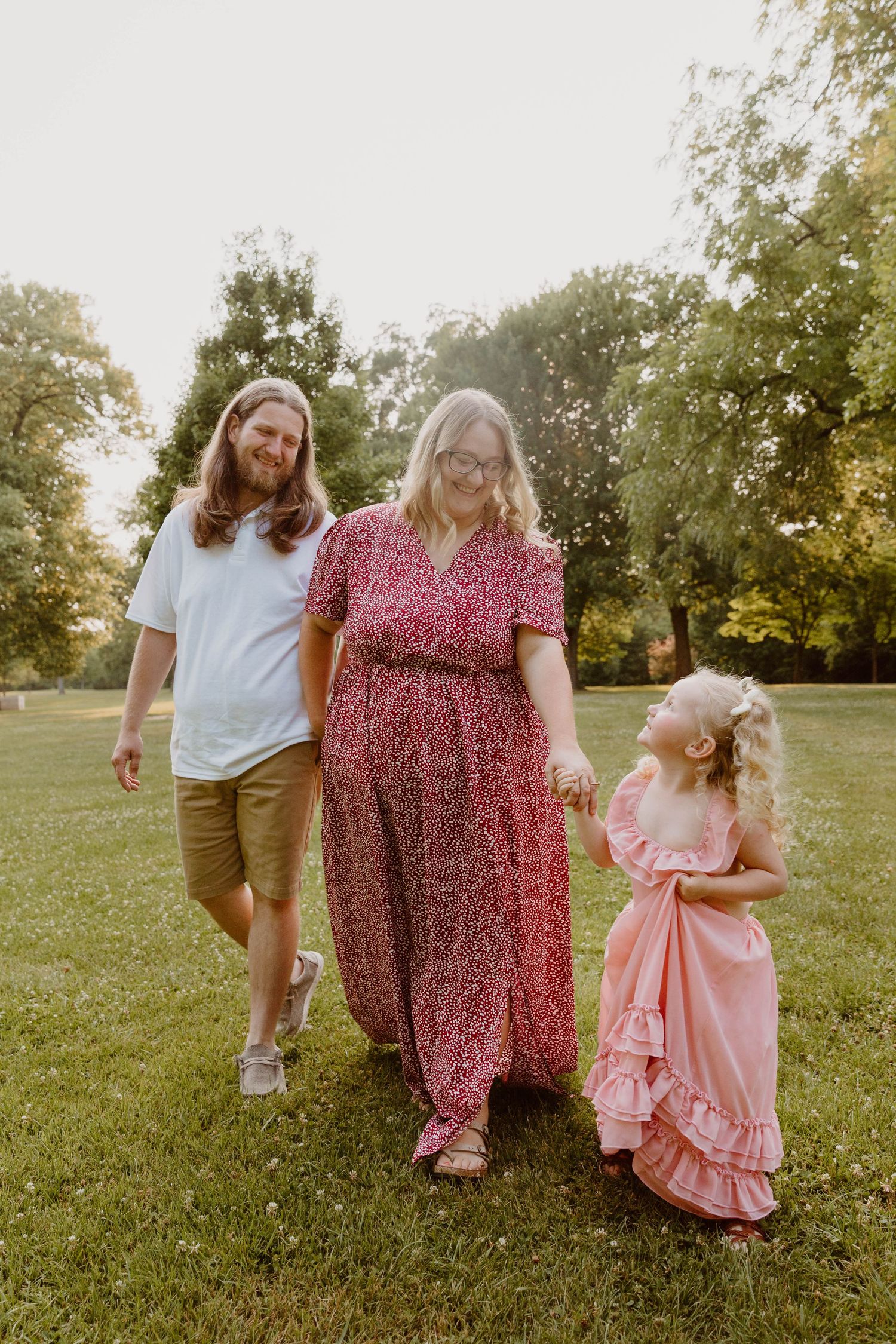 Family walking together in a sunny field with a young child in a pink dress.