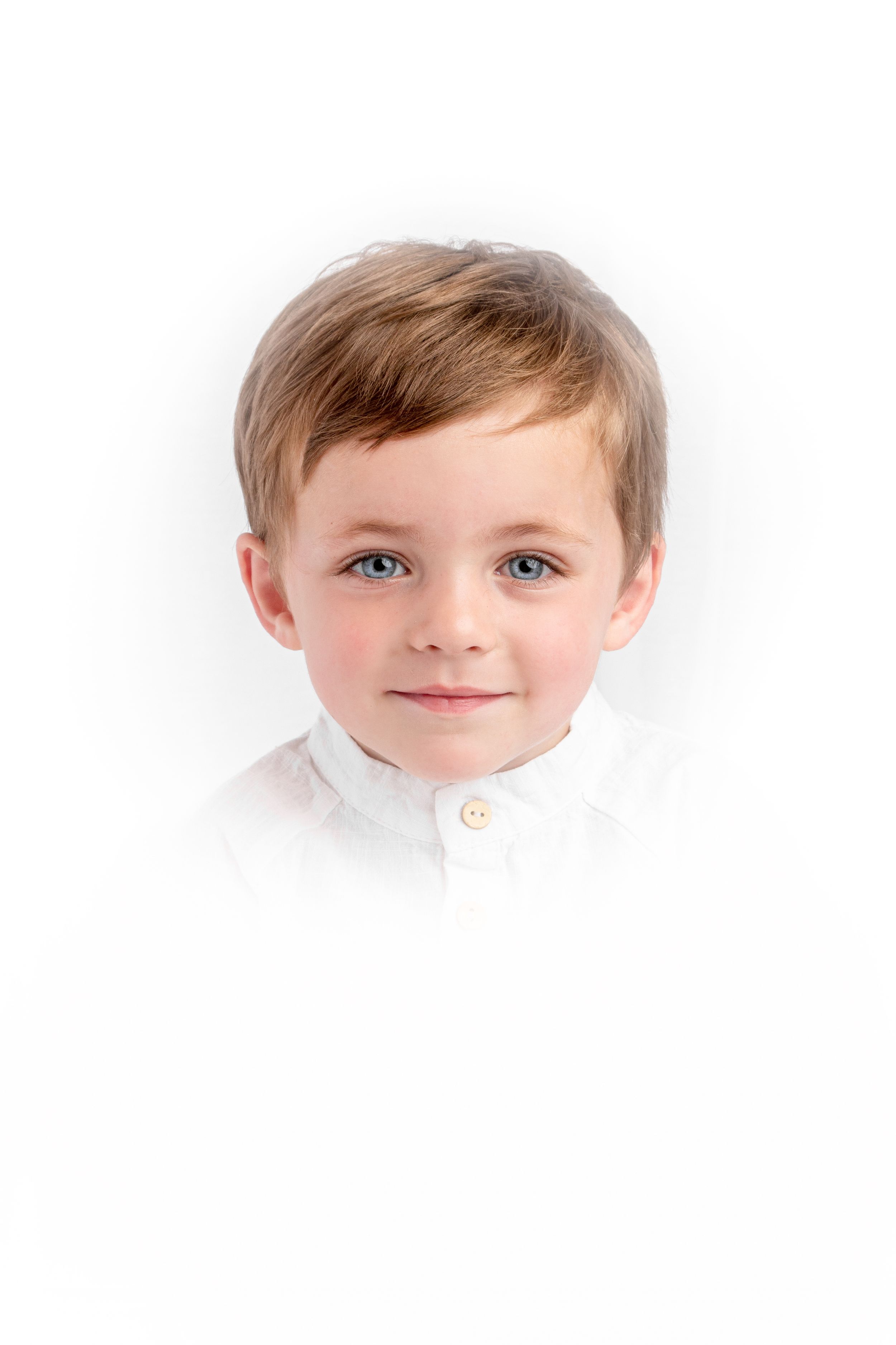 Heirloom style studio photograph of brown haired blued eyed boy in a white button collar shirt.