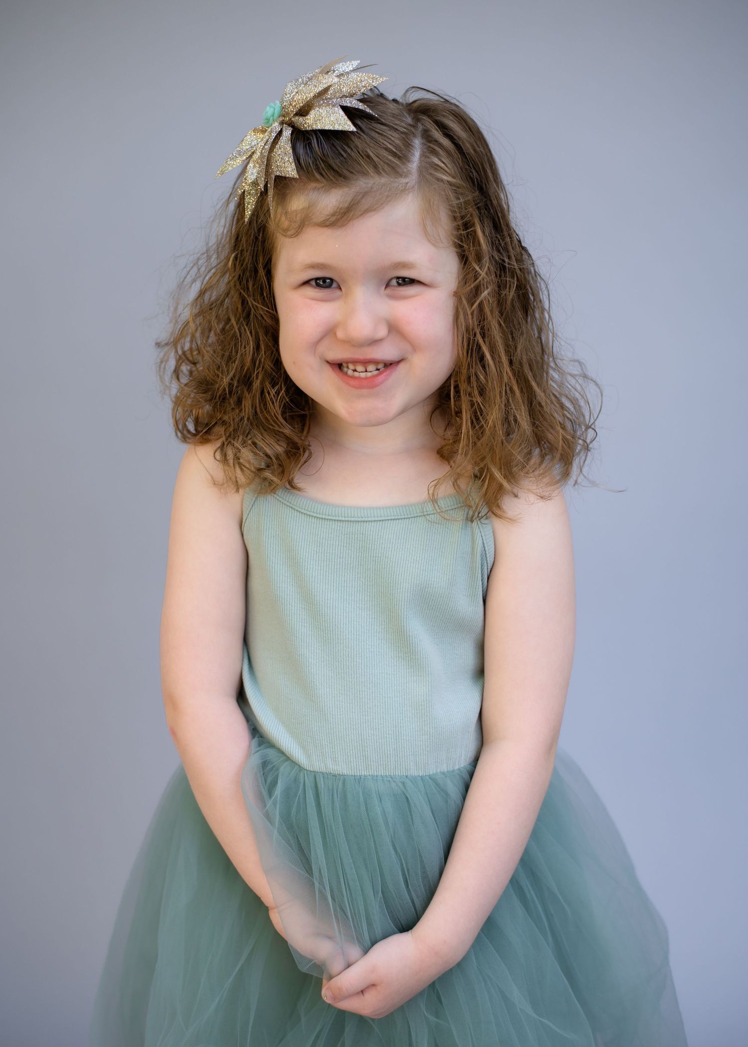 Child wearing mint dress and hair accessory smiles during studio portrait session.