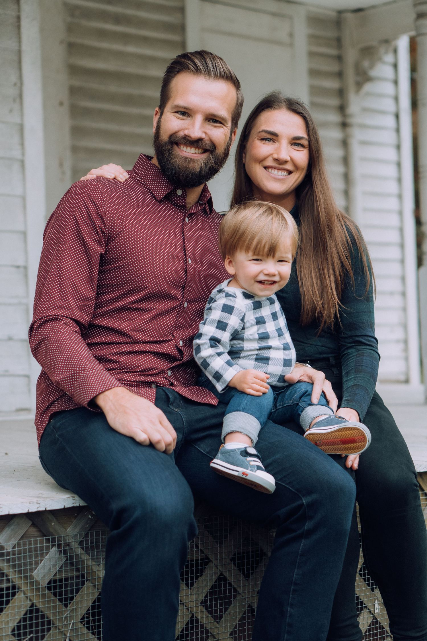 A family with a small toddler smile for the camera in a touching, natural portrait.