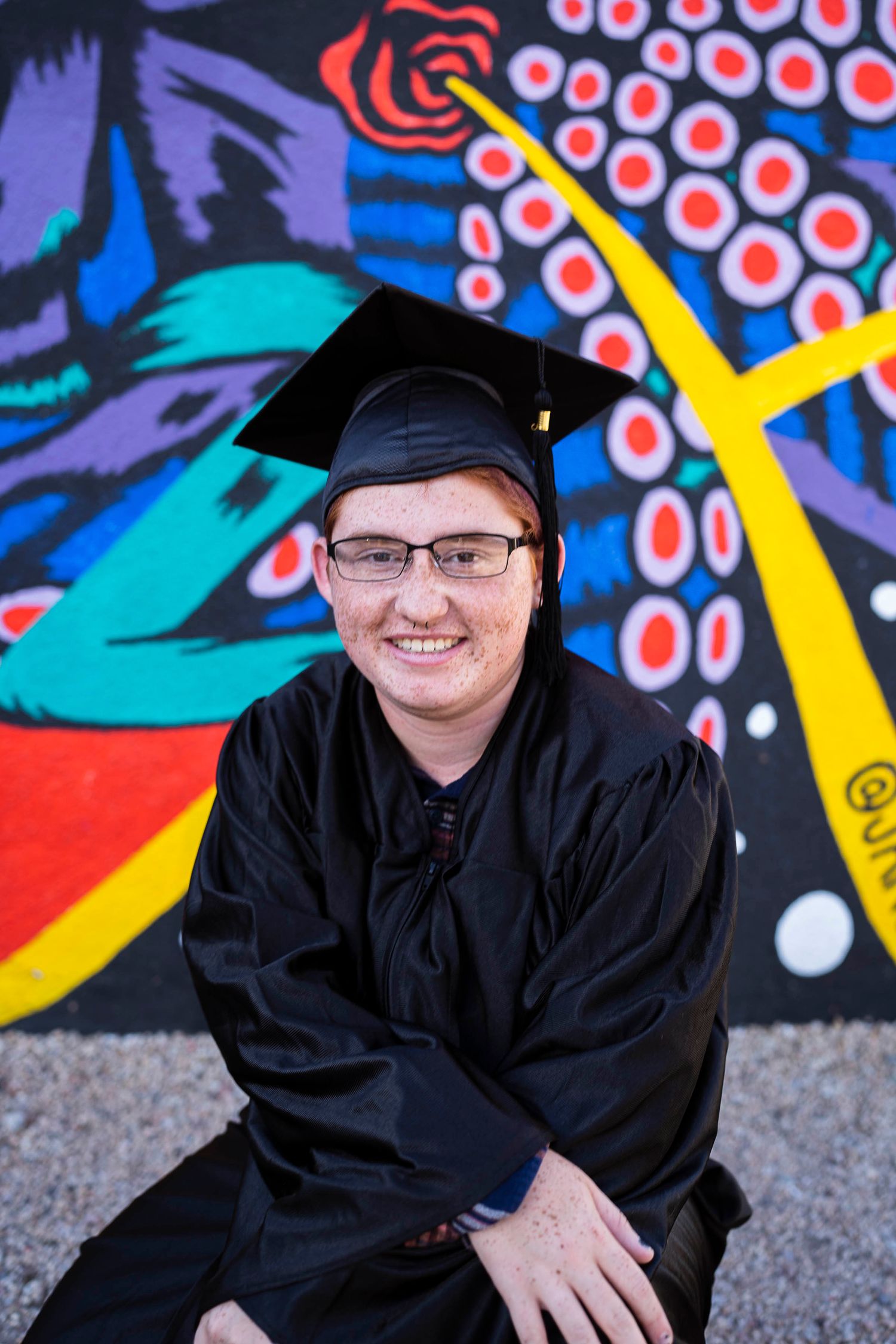 A senior boy posing in cap and gown in front of a mural in Phoenix, Arizona.