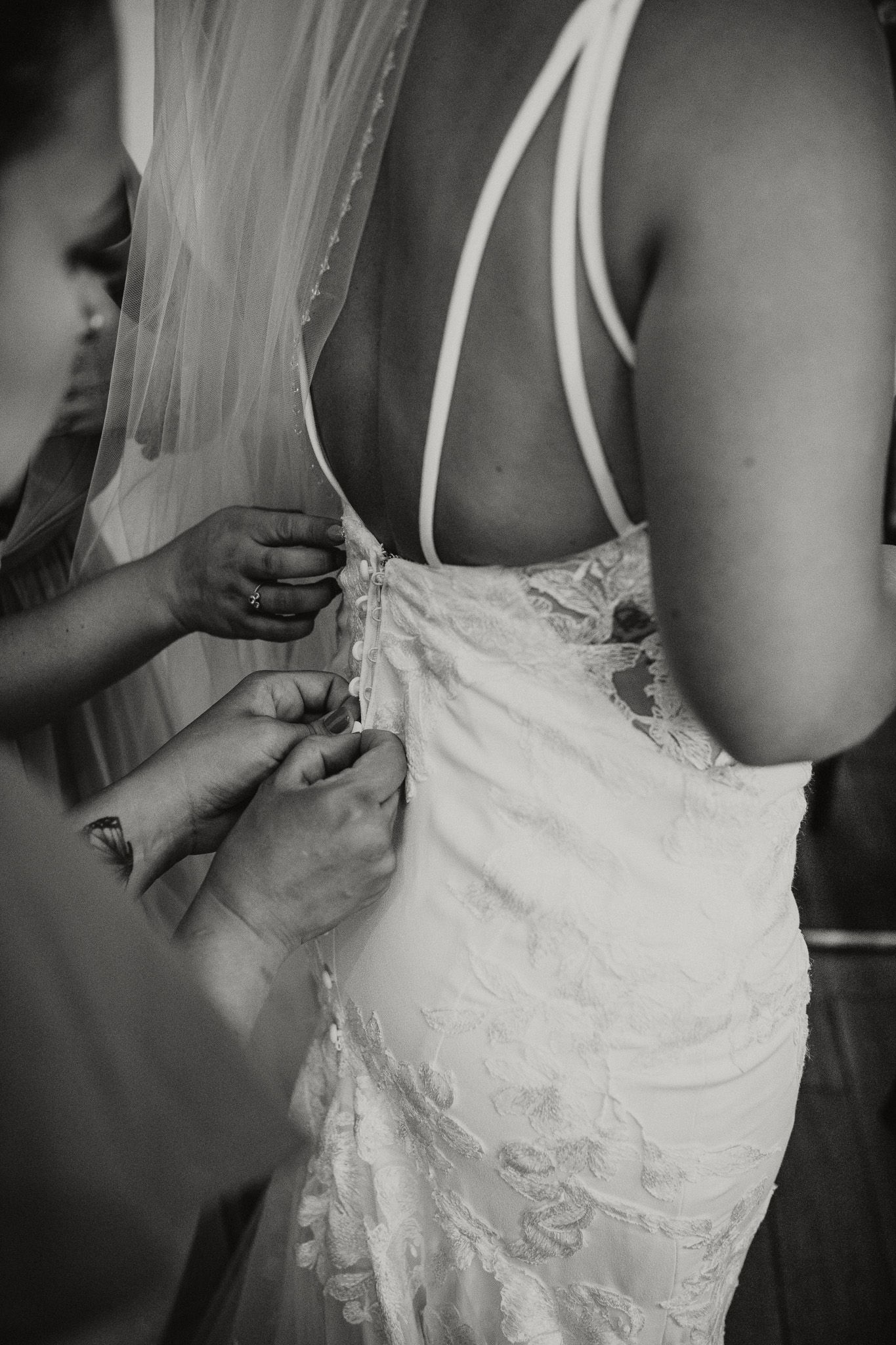 Black and white photo of bridesmaids doing up the buttons of brides dress in Okanagan.