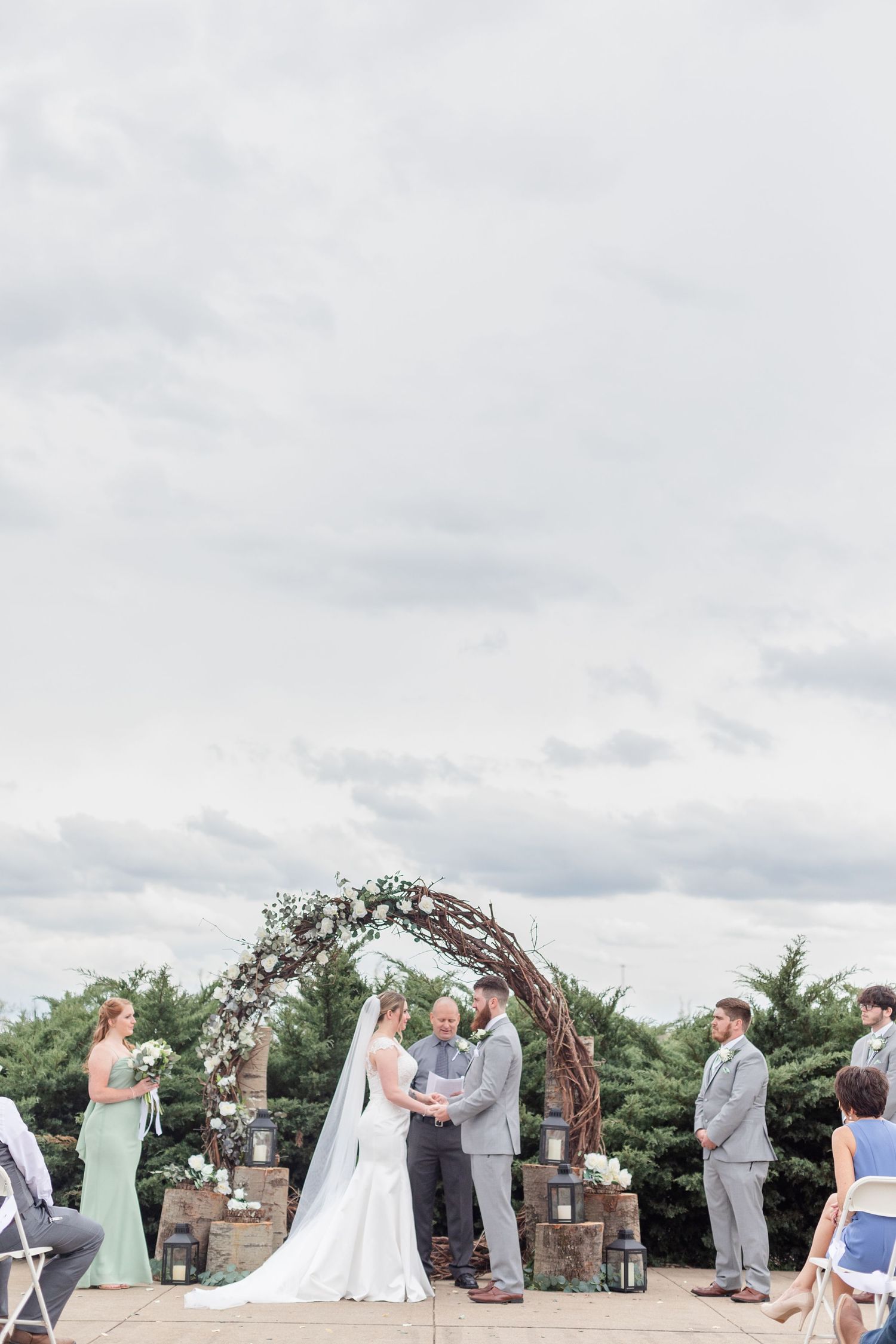 Wedding ceremony taking place under a floral arch with mint green and gray color scheme.