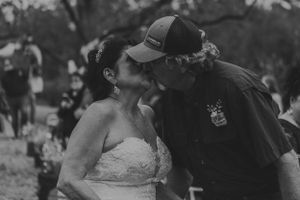 Black and white candid wedding moment captured outdoors under trees.