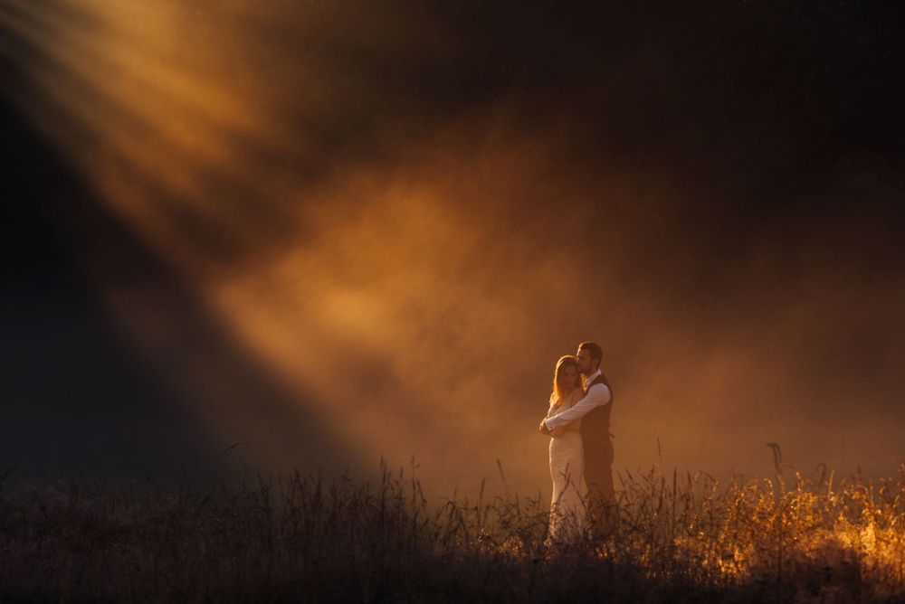 Dramatic silhouette of a couple embracing in a misty field at sunset with warm orange lighting.