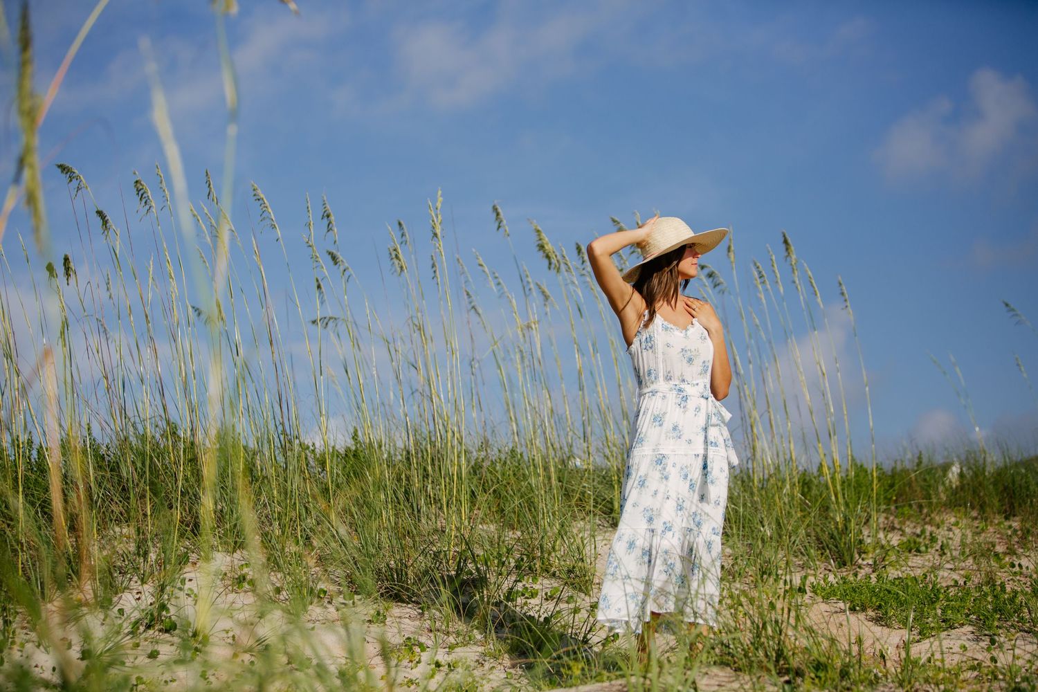 Dreamy summer portrait in a white dress among tall grass against blue sky.
