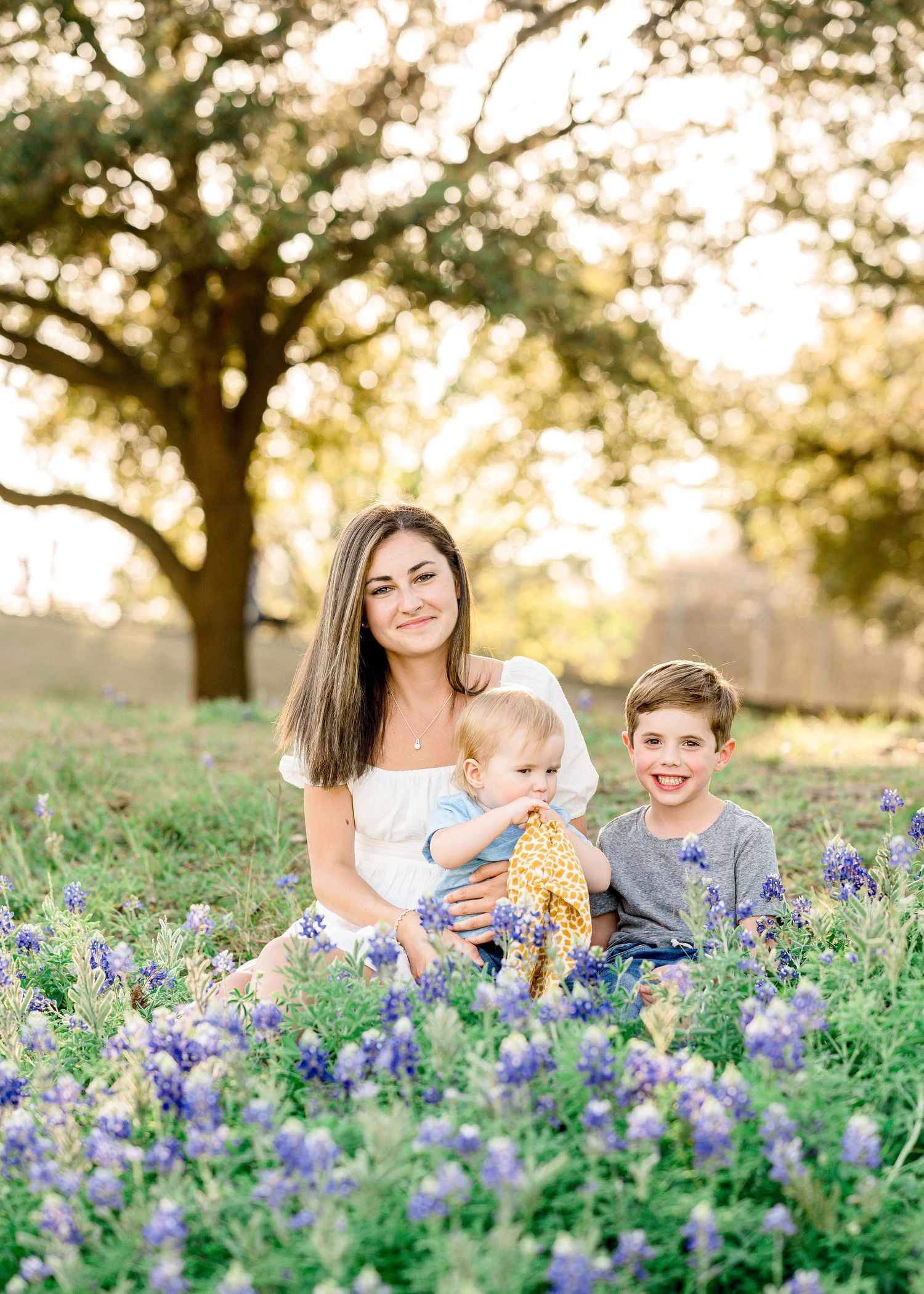 kids taking family portraits behind an oak tree and flowers girl wearing white shirt boy wearing grey shirt