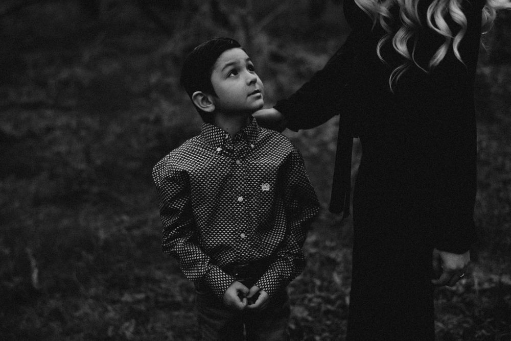 A moody black and white photo of a child looking up while standing next to someone in dark clothing.