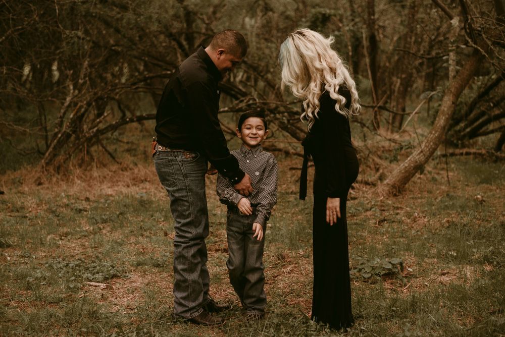 Three people share a tender moment while standing together in a forest clearing.