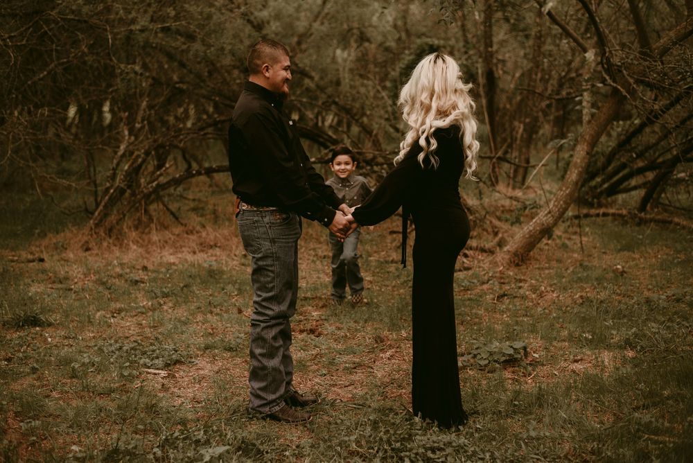 Three people holding hands in a circle formation outdoors surrounded by bare trees.
