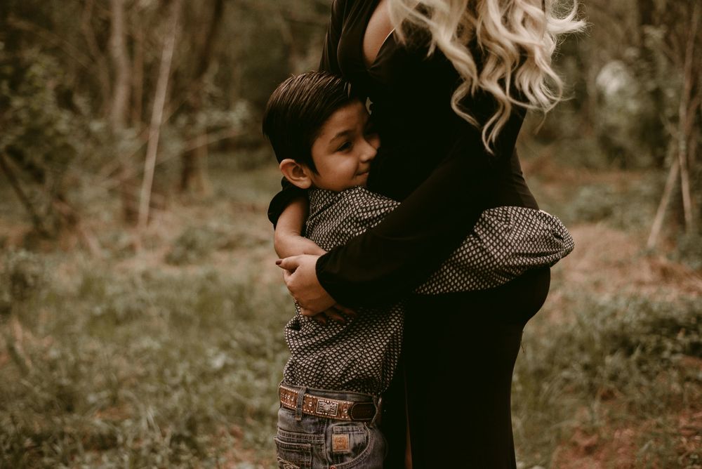 An intimate black and white portrait of a tender hug between parent and child in a woodland setting.