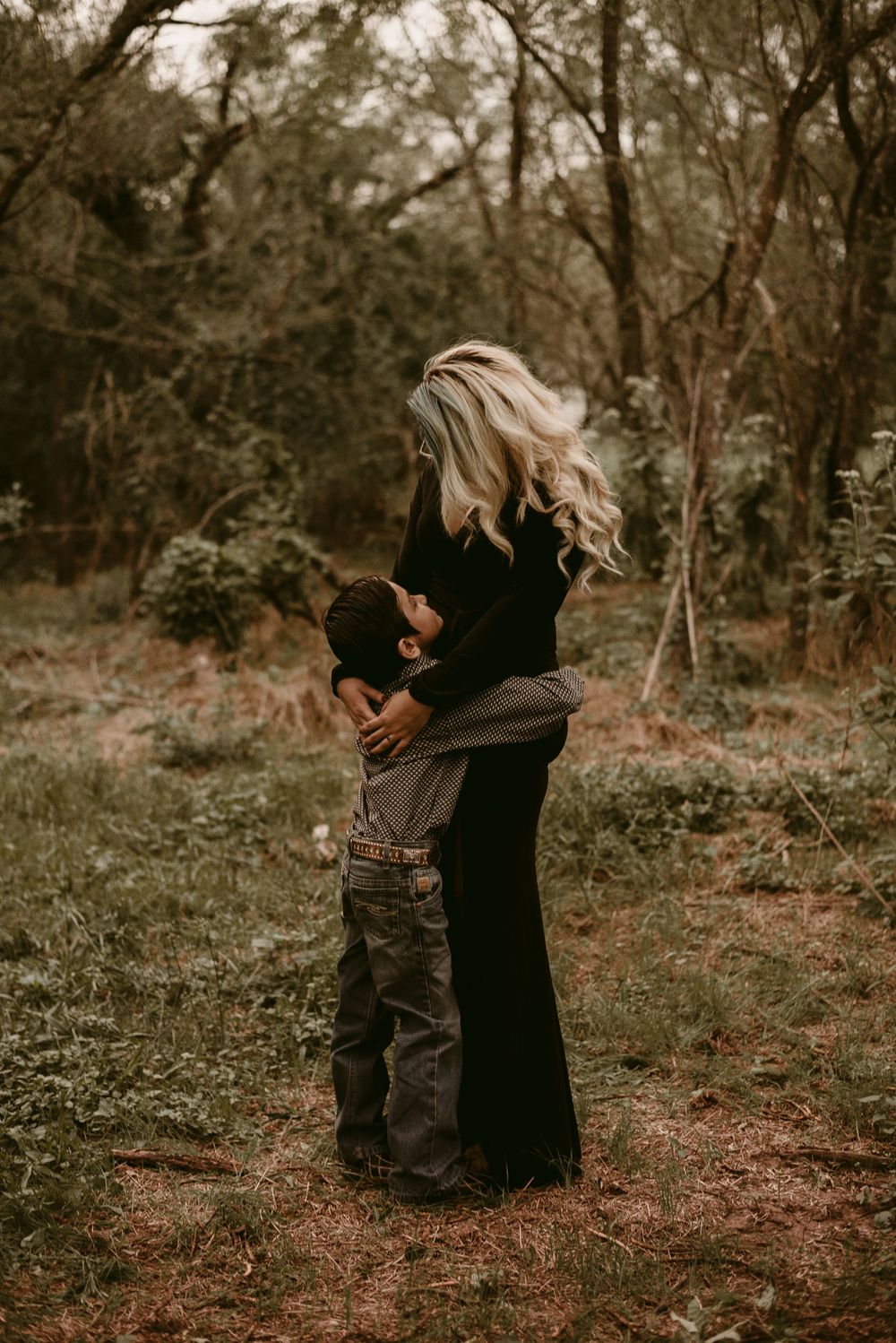 A warm embrace between two people standing on a forest path during golden hour.