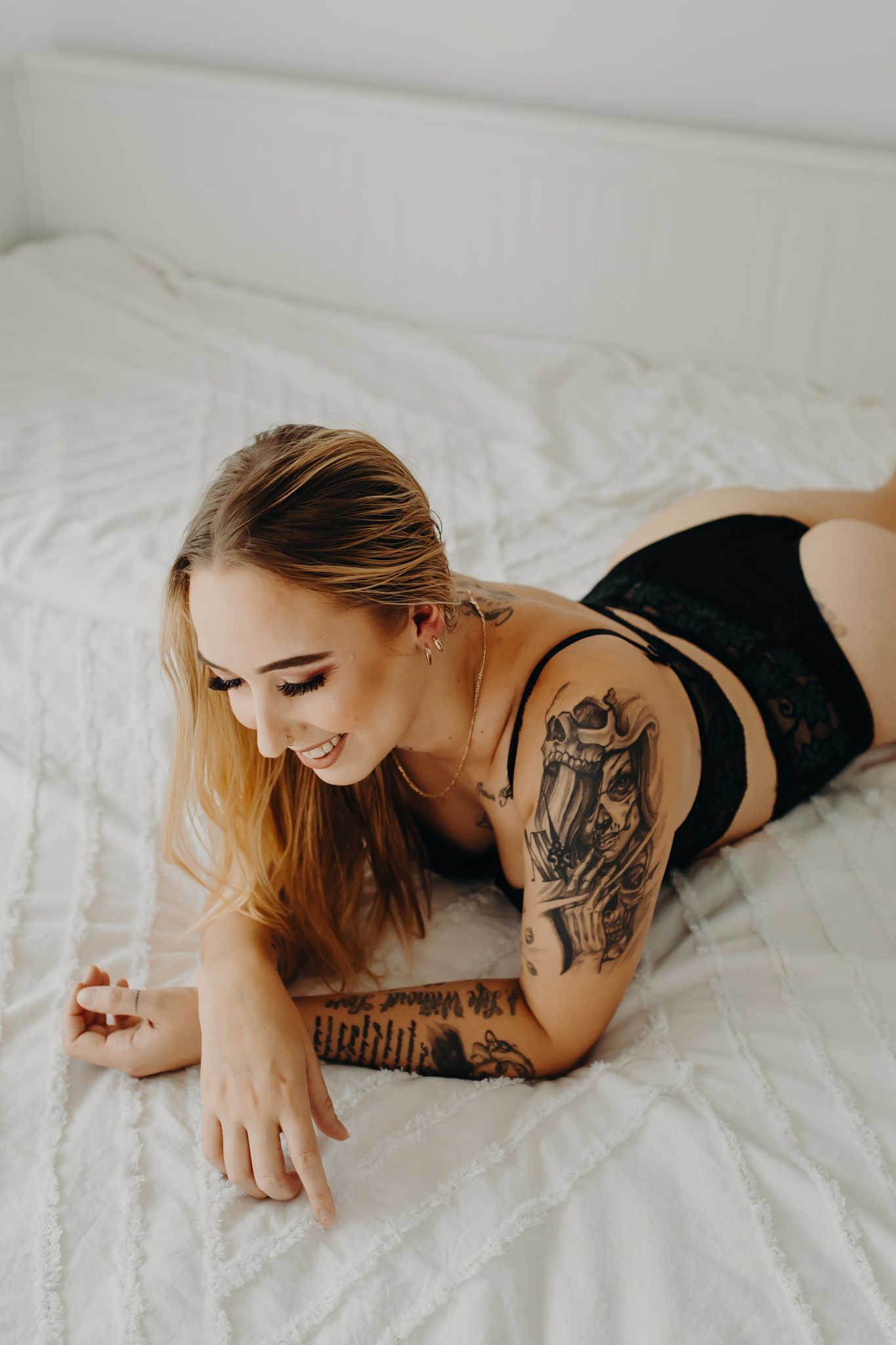 Portrait on white bedding showing artistic tattoo designs.