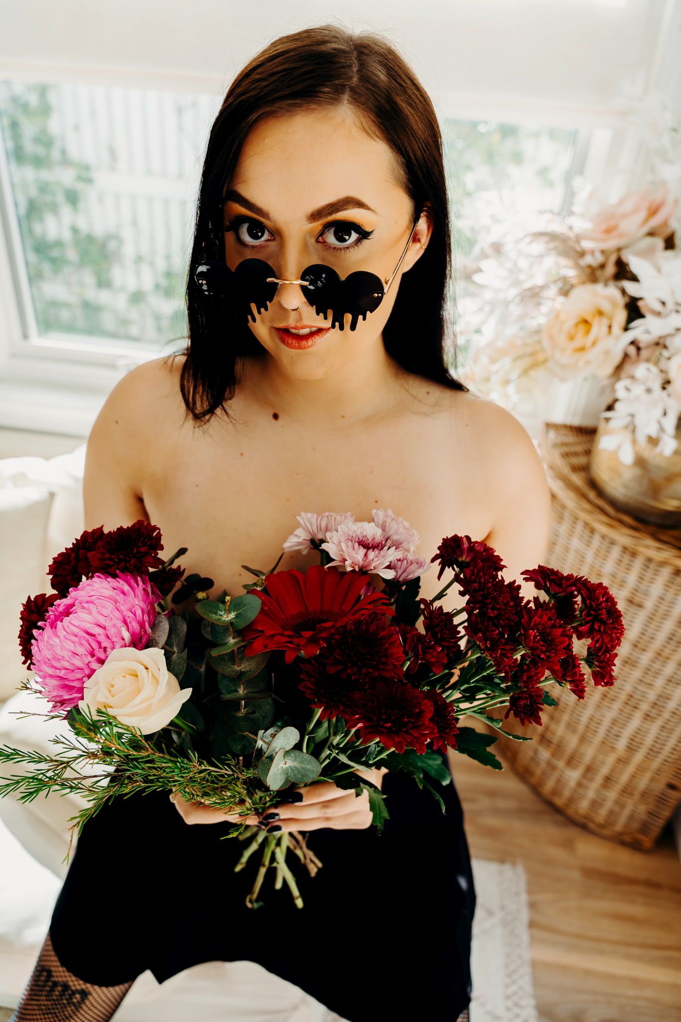 Person holding colorful bouquet of roses and flowers wearing black dress with butterfly face paint.