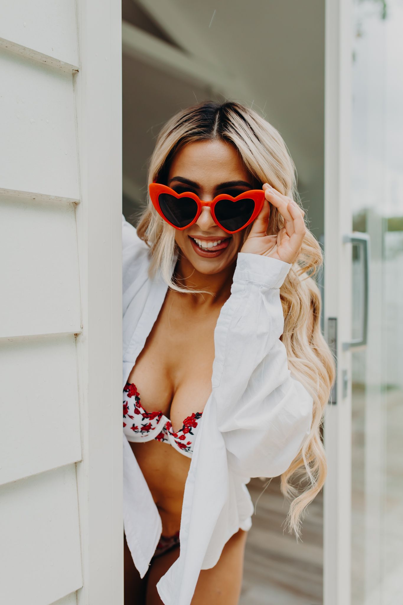 Playful portrait featuring heart-shaped red sunglasses and white button down shirt in casual boudoir style.
