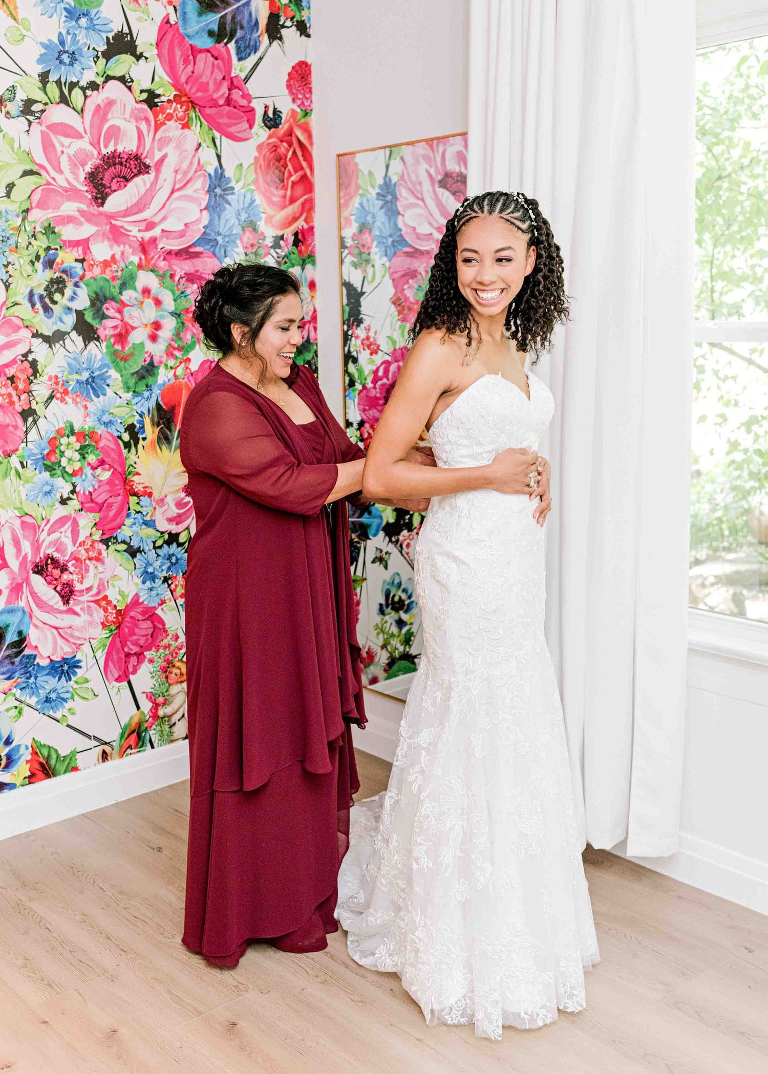 Wedding dress fitting moment against vibrant floral wallpaper backdrop.