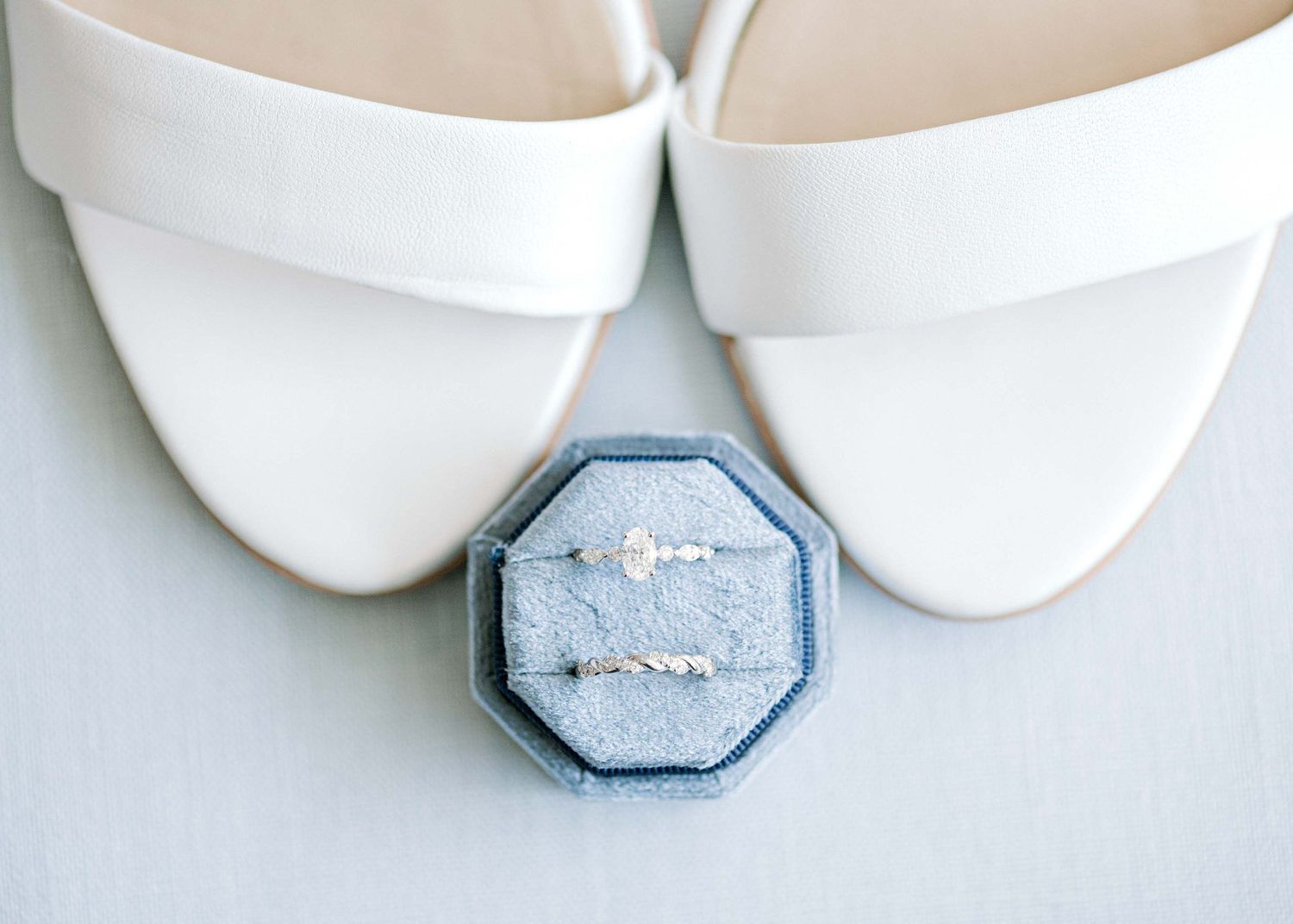 White bridal sandals with blue velvet ring box containing delicate engagement ring.