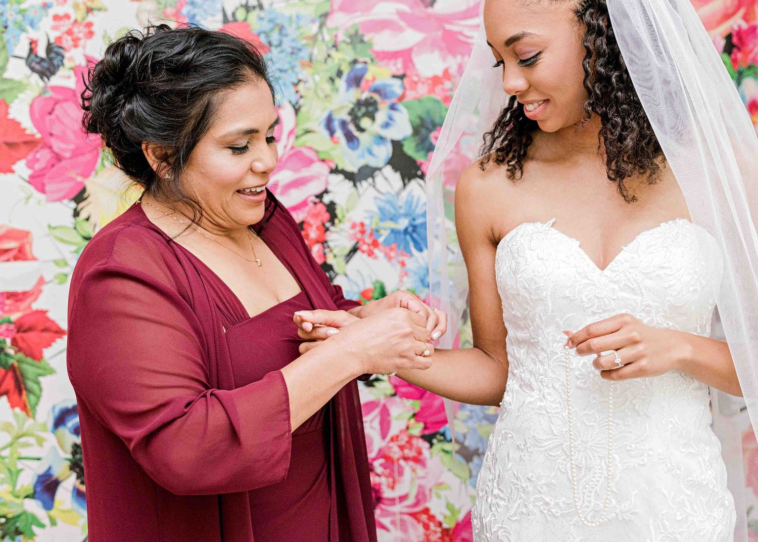 Wedding preparation moment with burgundy-dressed assistant helping with bridal accessories.