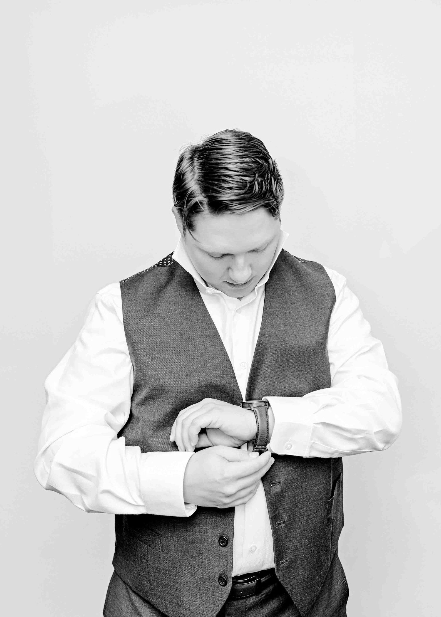 Black and white portrait of groom adjusting cuffs while getting ready.
