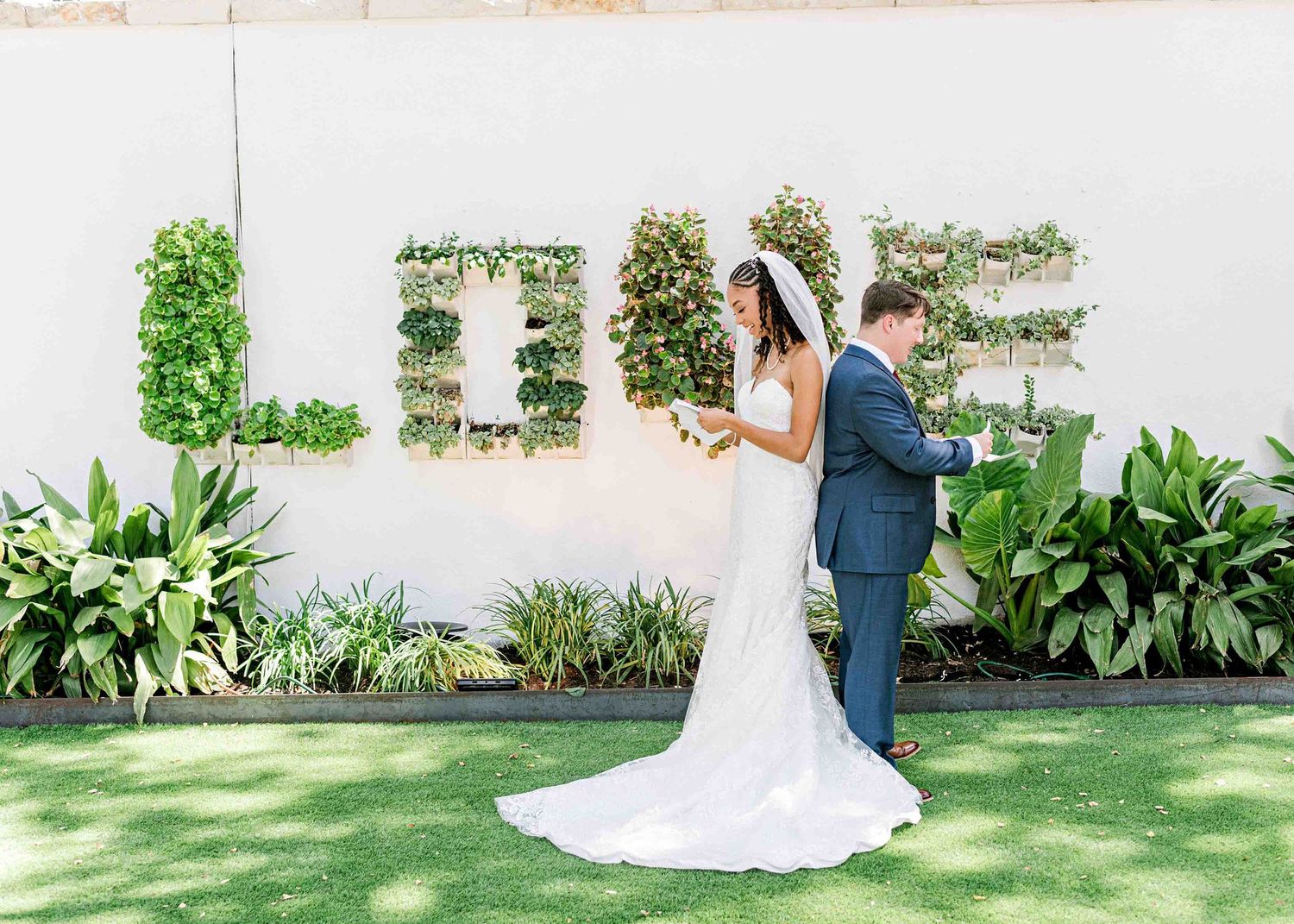 A romantic outdoor wedding ceremony featuring a floral LOVE sign display on a white wall with lush greenery.