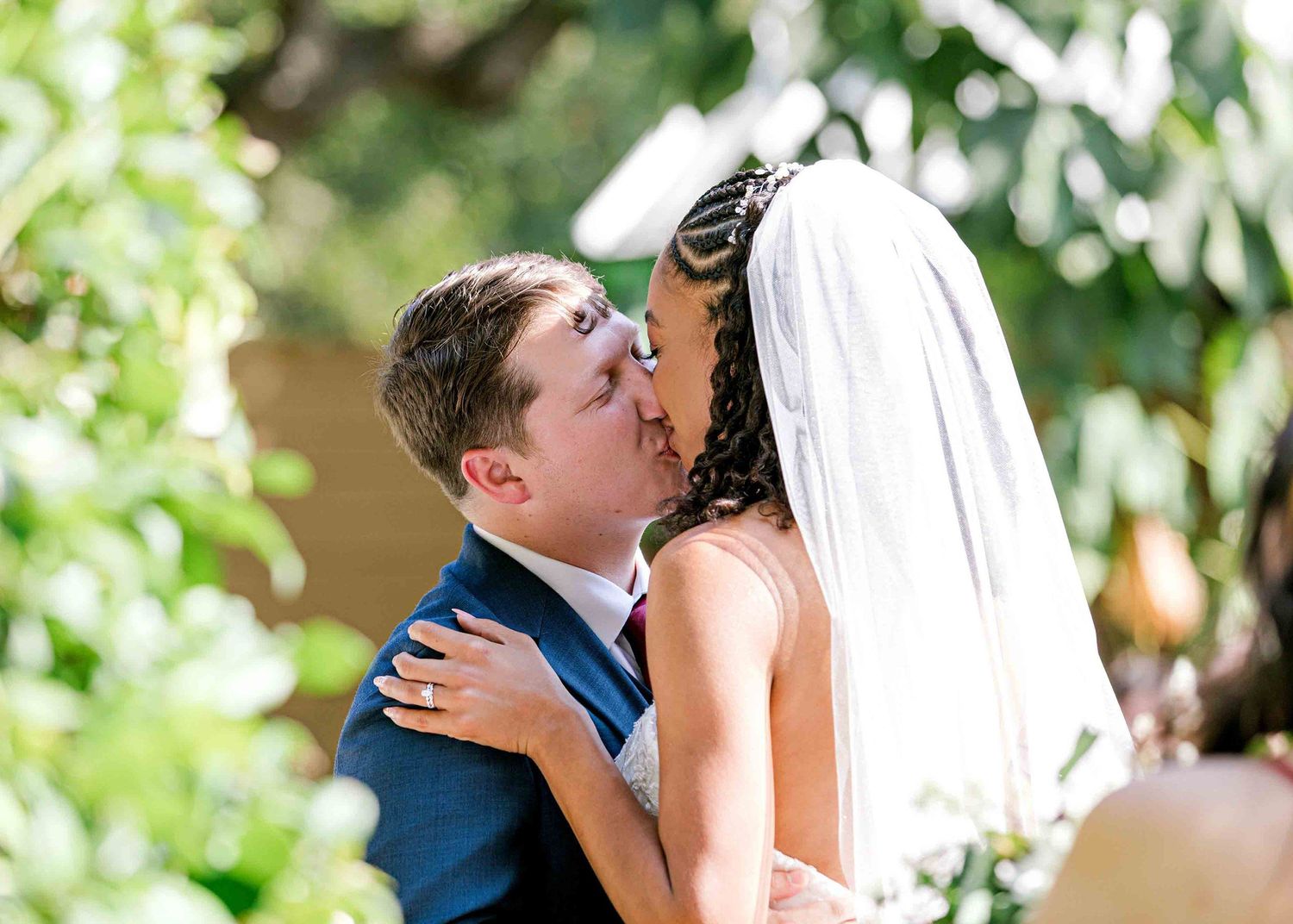 A tender kiss between newlyweds under a garden arch draped with greenery.