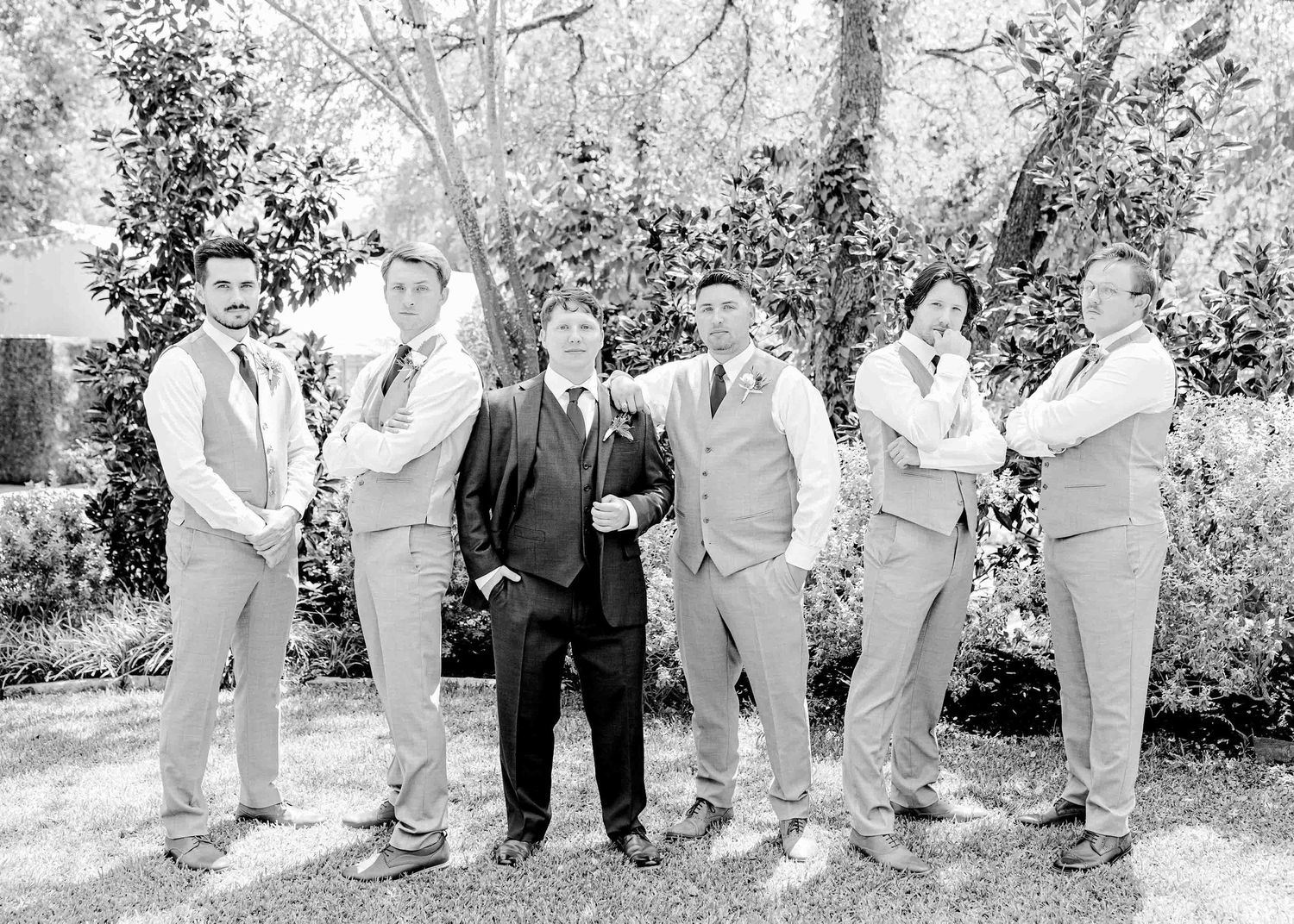 Vintage-style black and white photo of wedding party in light suits posing outdoors.
