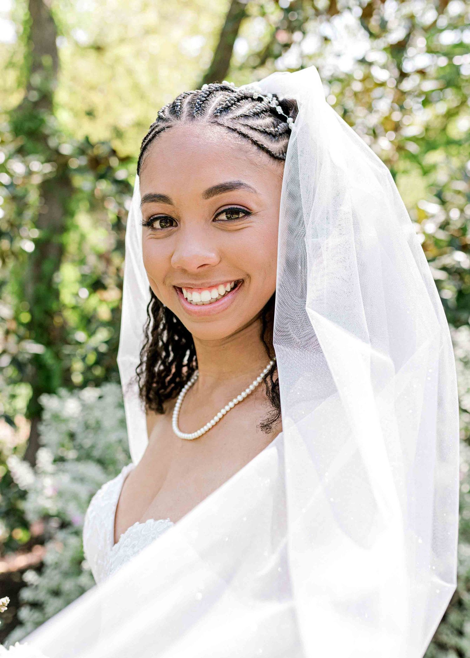 Bridal portrait in a garden setting featuring an elegant white veil and pearl necklace.